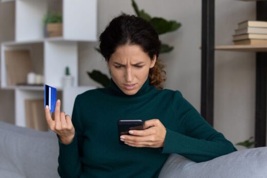 femme étonnée devant son smartphone avec carte bancaire dans la main